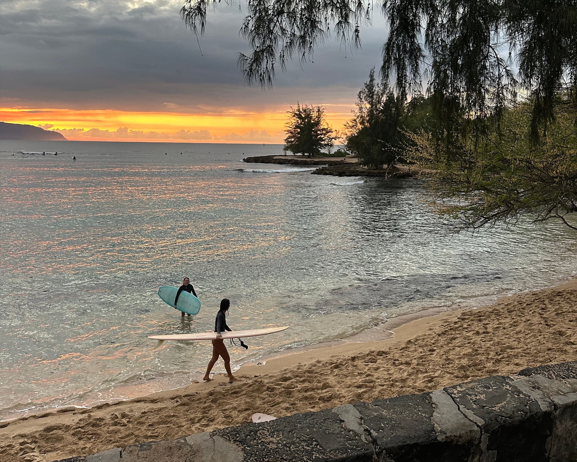 Two surfers coming out of the ocean at sunset.