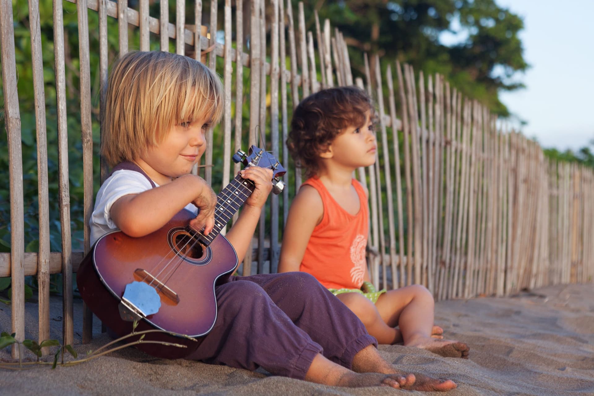kids playing ukulele on the beach against a fence
