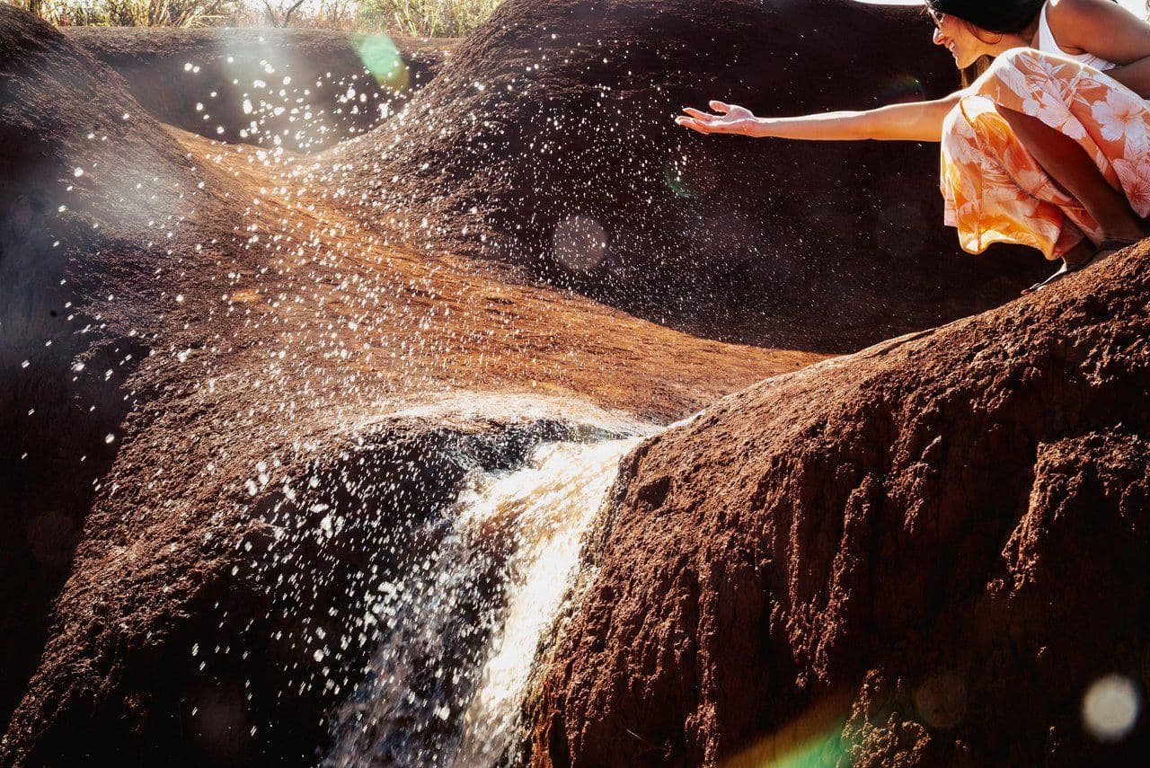 A girl splashing water from a waterfall at waimea canyon.