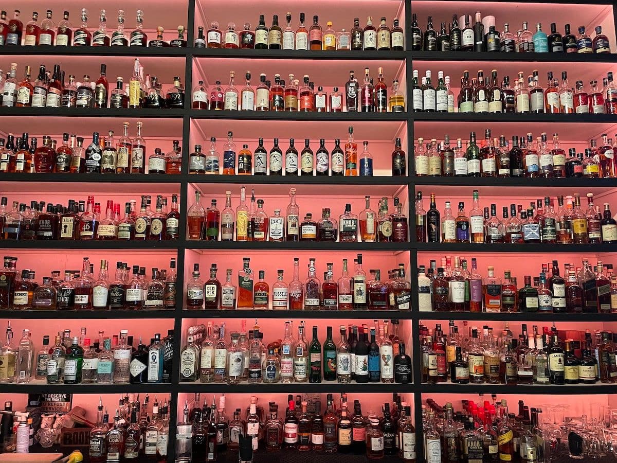 a wall of spirits, liquor bottles on shelves with pink backlighting
