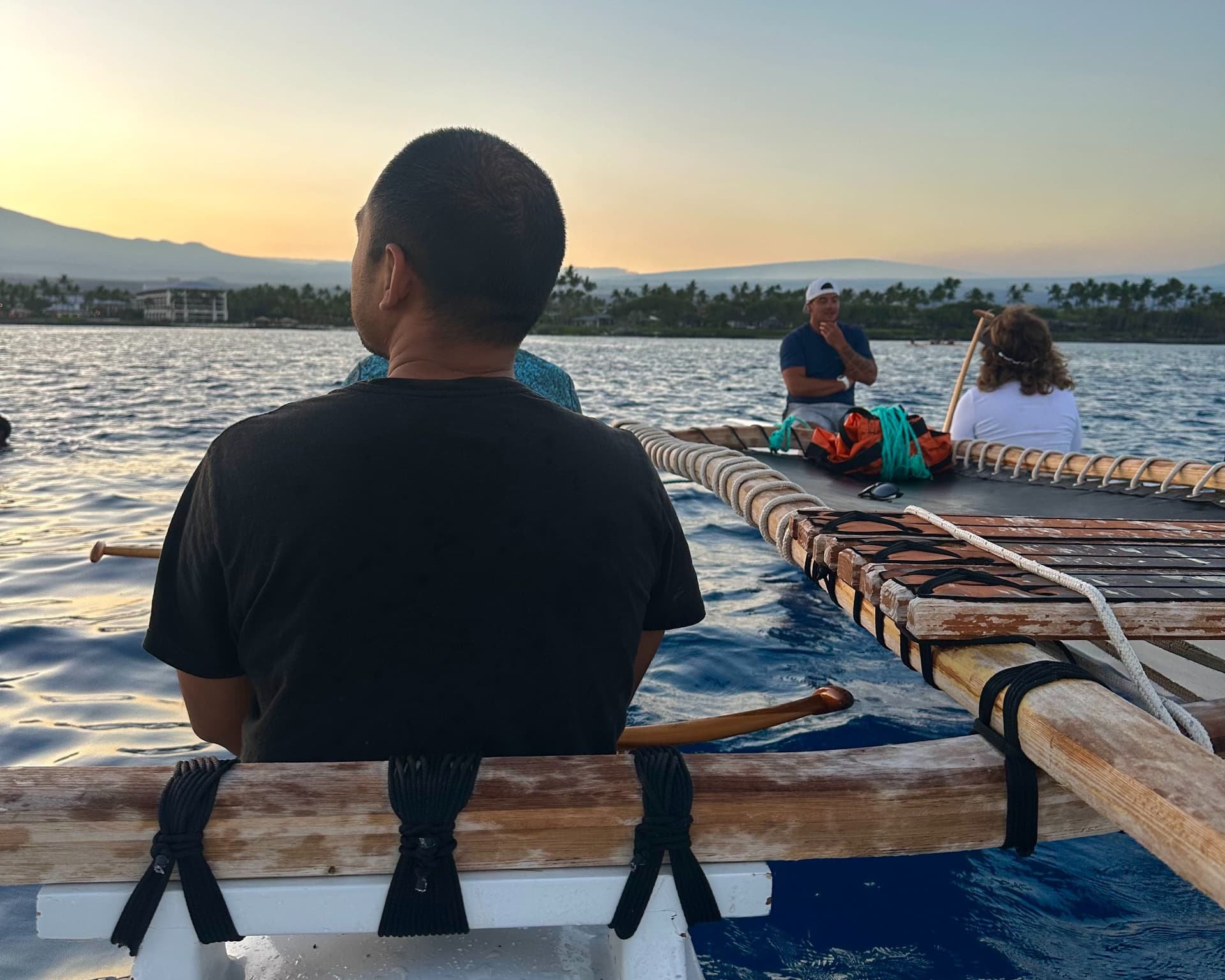 people riding in an outrigger canoe during sunrise