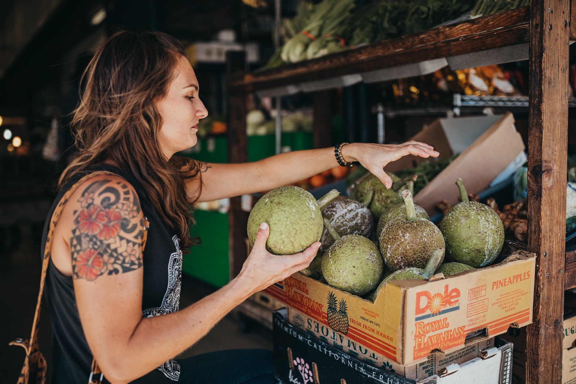 Woman selecting breadfruit from a box at an outdoor market