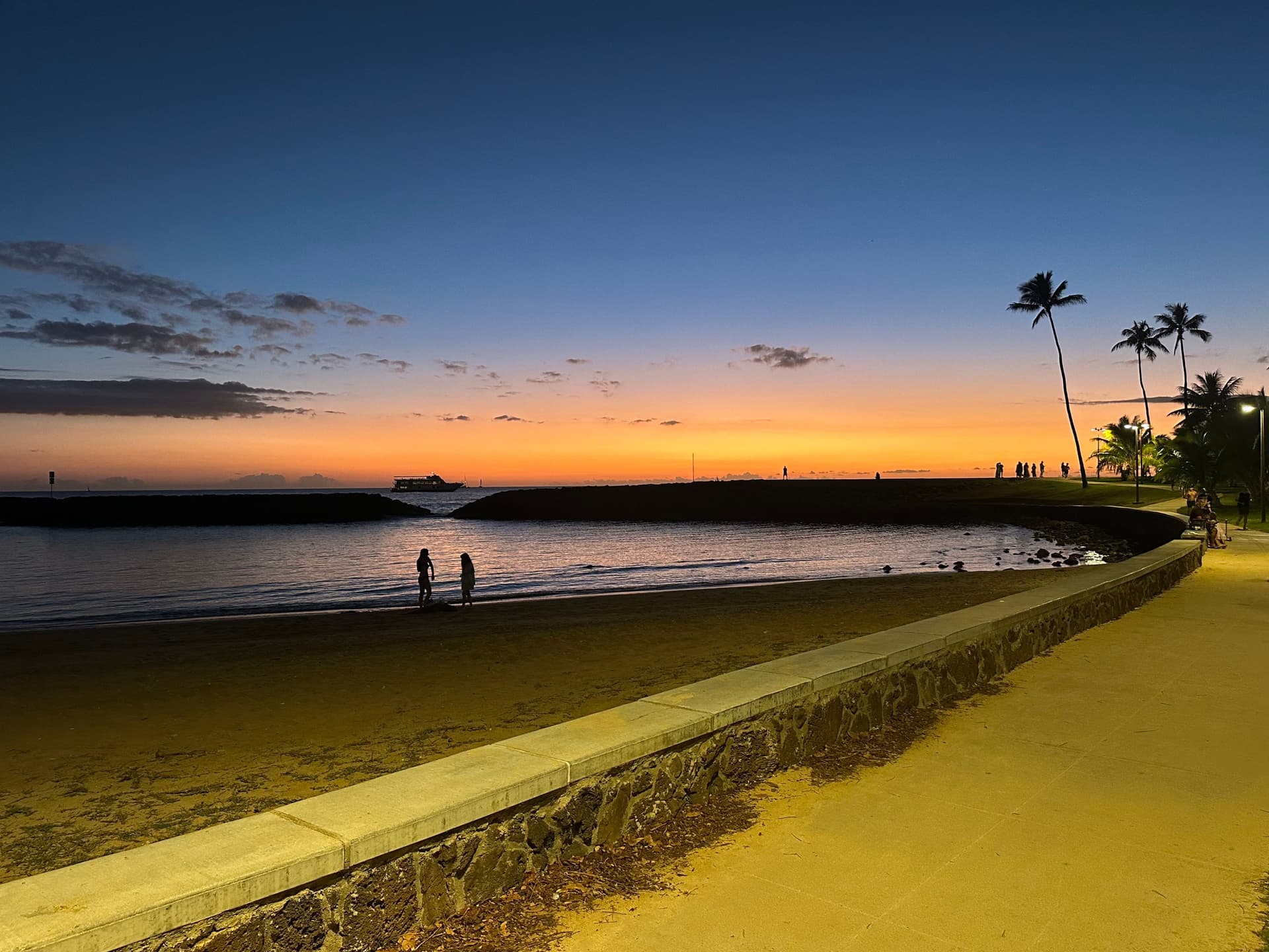 Two people walking down the beach in front of the lagoon at Magic Island during sunset. Oahu, Hawaii.