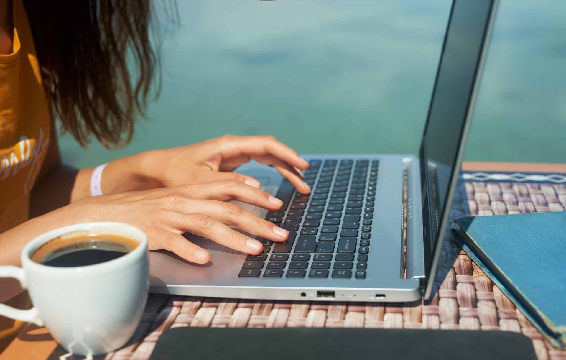 woman working at a laptop by the pool with a cup of coffee