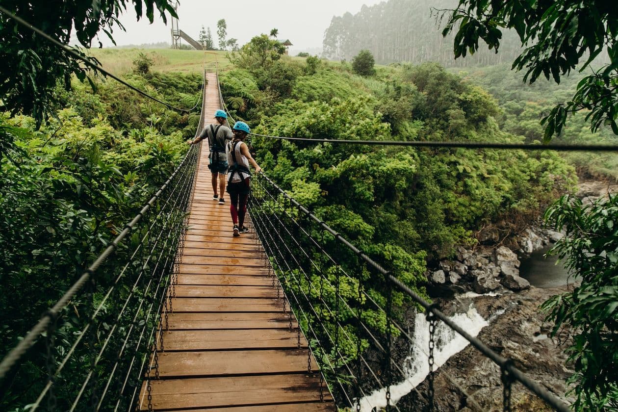 Two people walking across a bridge in a valley in hawaii.