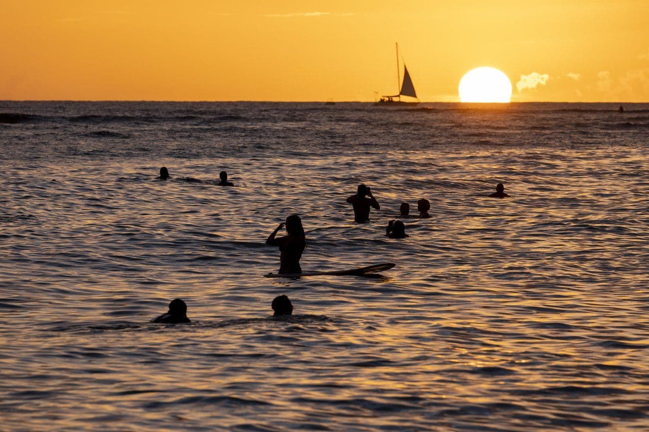 Sunset over the ocean with surfers in the water in Waikiki, Hawaii.