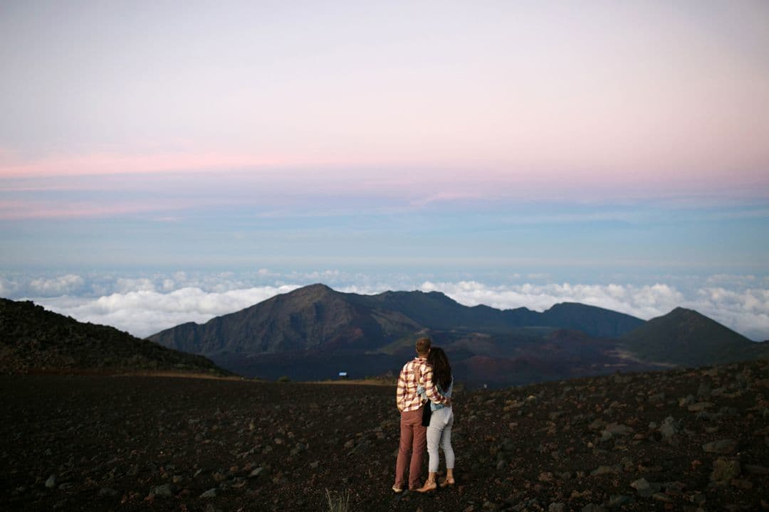 A couple standing at the summit of Haleakalā at sunrise on Maui, Hawaii.
